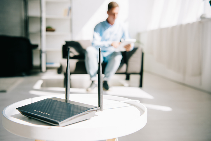selective focus of black plugged router on white table and businessman sitting on sofa